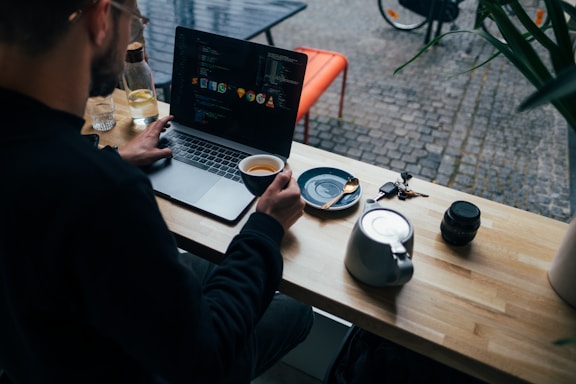 A friendly web developer working at a desk with code on the screen and a cup of coffee nearby.