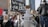 A crowd of people, some holding signs, are participating in a protest. Among them is a person dressed in a robot costume with a sign that reads 'Wir sind die Bots.' The atmosphere is busy and filled with various signs with messages related to digital rights.
