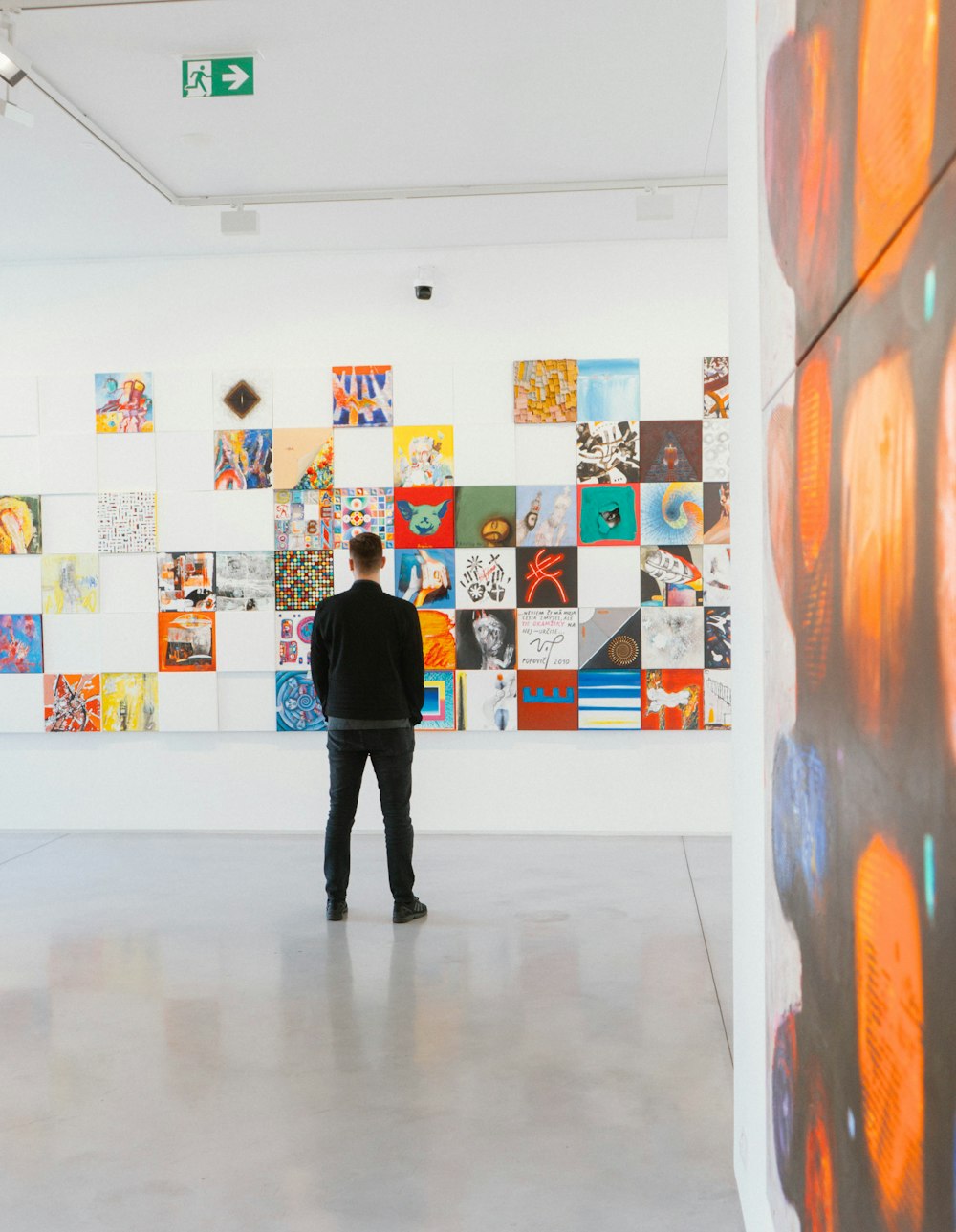 Hombre con camisa negra de manga larga y pantalones negros de pie detrás de pinturas abstractas