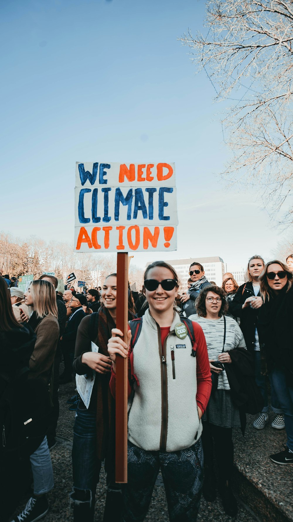 standing and smiling woman holding We Need Climate Action! sign