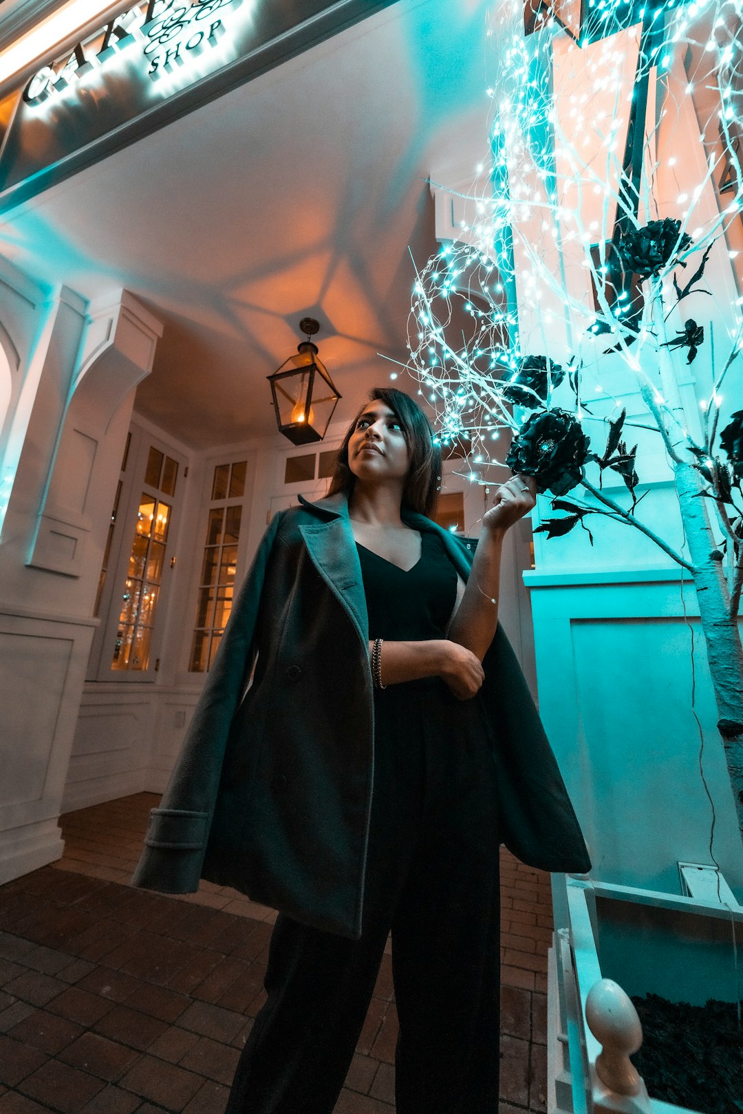 standing woman wearing coat standing beside plant with string lights at night