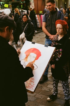standing man painting standing girl wearing red hat during daytime