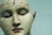 A detailed and realistic sculpture of a human head with anatomical features. The surface is inscribed with words and markings that appear to categorize different areas of the brain. The model is presented with closed eyes, giving it a calm and serene expression.