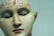 A detailed and realistic sculpture of a human head with anatomical features. The surface is inscribed with words and markings that appear to categorize different areas of the brain. The model is presented with closed eyes, giving it a calm and serene expression.