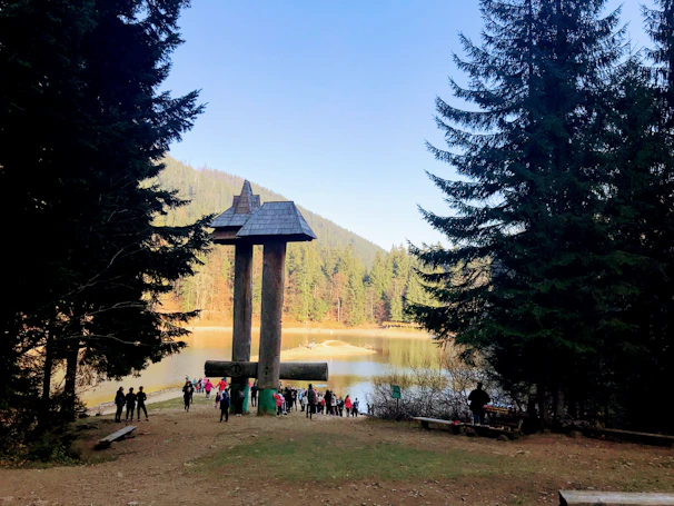 Wide shot of festival attendees watching an artist shape a large wooden statue outdoors.