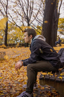 A colorful backpack hanging on a park bench with autumn leaves scattered around.