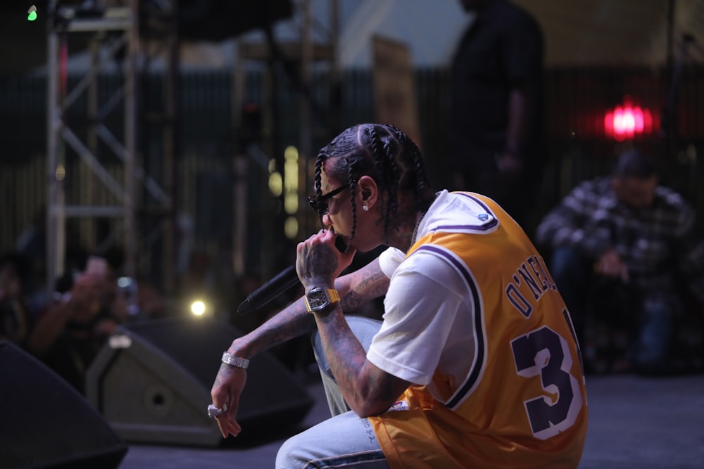 man in yellow jersey sitting while holding microphone on the stage