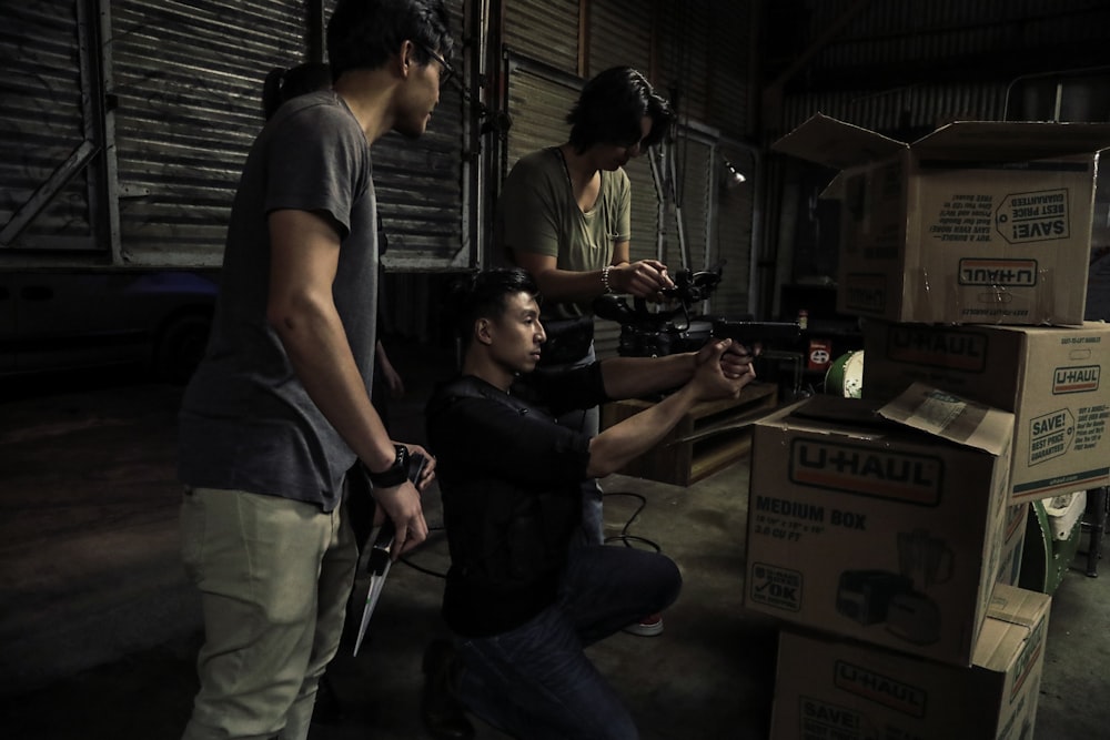 two man standing in front of man sitting in front of box inside building