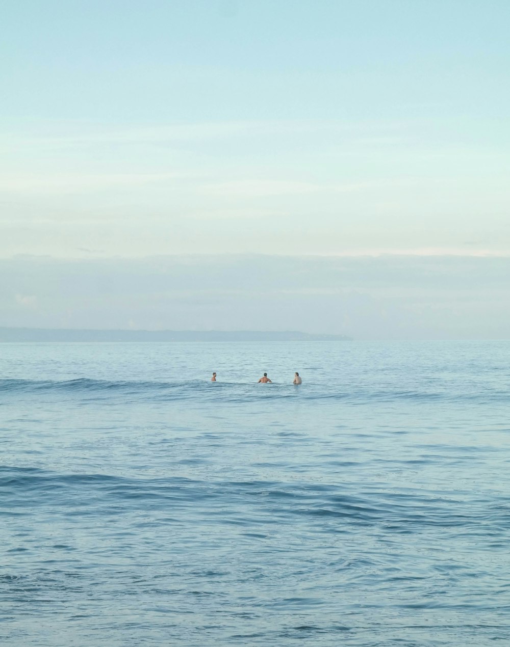 three people on blue body of water viewing mountain under blue and white sky during daytime