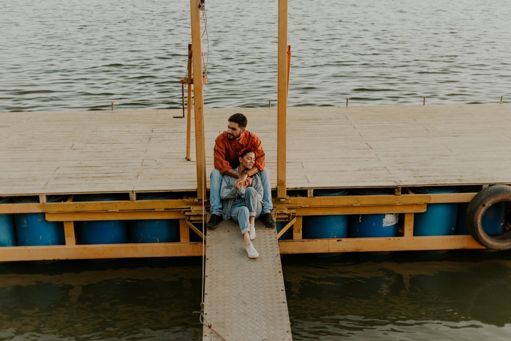 couple sitting on dock surround by body of water during daytime]