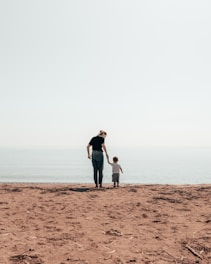 woman and toddler standing beside seashore during daytime