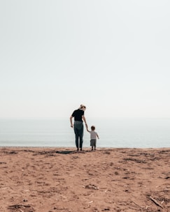 woman and toddler standing beside seashore during daytime