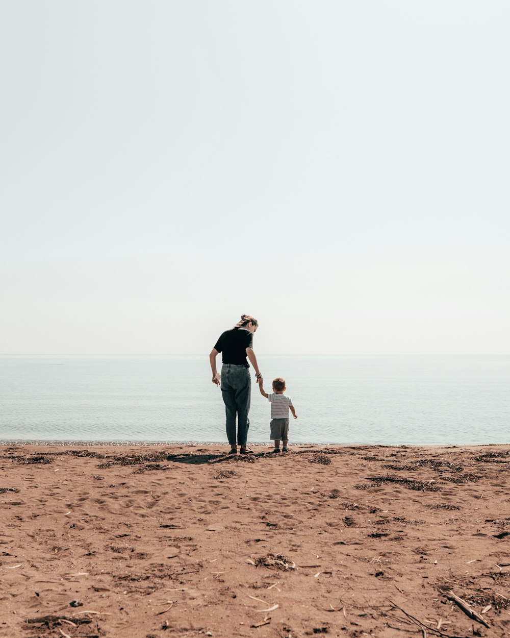 woman and toddler standing beside seashore during daytime