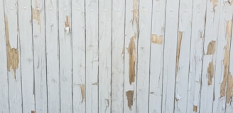 Weathered wooden boards with peeling white paint exposing patches of the natural wood underneath. Vertical alignment creates a pattern of alternating painted and bare surface areas.