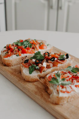 Rustic wooden board showcasing assorted bruschetta topped with ripe tomatoes, basil, and drizzled olive oil.