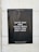 A black poster with white text is taped to a light-colored wall. The text on the poster reads, 'You've read more social media posts than book pages.' The background of the poster is plain black, creating a stark contrast with the white lettering. The poster contains a website address at the bottom, inviting viewers to visit.