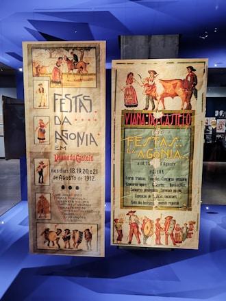 Two vintage posters advertising the Festas da Agonia event in Viana do Castelo, dated August 1912. The posters feature traditional illustrations, including people in cultural attire, a horse, and a cow. The left poster highlights activities such as horse competitions, parades, and serenades. The right poster emphasizes livestock contests and fireworks, with vibrant illustrations surrounding the text.