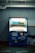 A dimly lit vending machine stands against a plain wall, stocked with rows of bottled beverages, including water and isotonic drinks. The machine is predominantly blue with illuminated sections highlighting the available products and a signage that reads 'Bonaqua BonACTIVE Isotonic'.