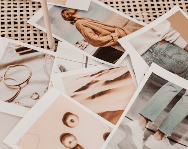 A collection of photographs scattered on a wicker surface. The images depict various subjects, including a person wearing a brown sweater, a pair of jeans with white sneakers, several pieces of jewelry like rings and earrings, and abstract close-ups of fabric and apples. The overall tone appears warm and vintage.
