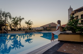 Sunlit model in flowing white resort dress by the poolside, palm shadows dancing on her skin.
