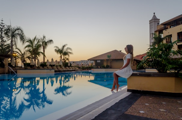 Sunlit model in flowing white resort dress by the poolside, palm shadows dancing on her skin.