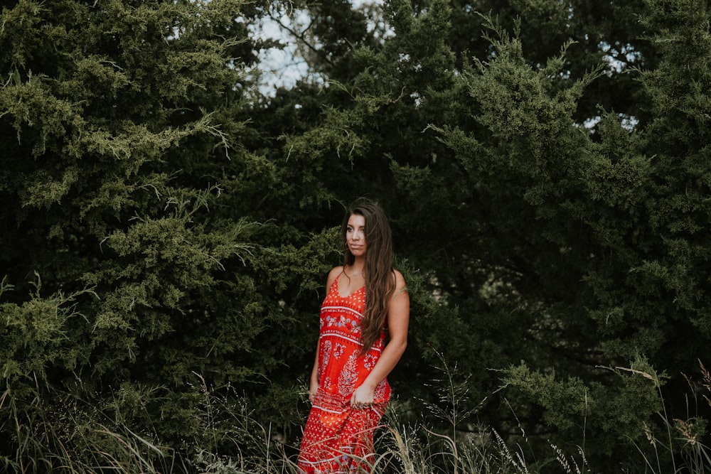woman in red spaghetti-strap dress standing beside green trees
