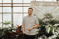 man in grey crew-neck top holding sunglasses standing near plants