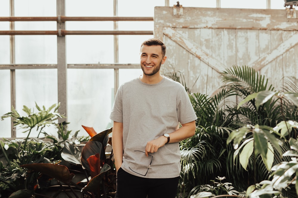 man in grey crew-neck top holding sunglasses standing near plants