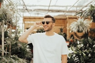 A farmer smiling while inspecting vibrant plants in a sunlit greenhouse.