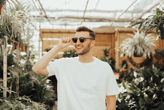 A farmer smiling while inspecting vibrant plants in a sunlit greenhouse.