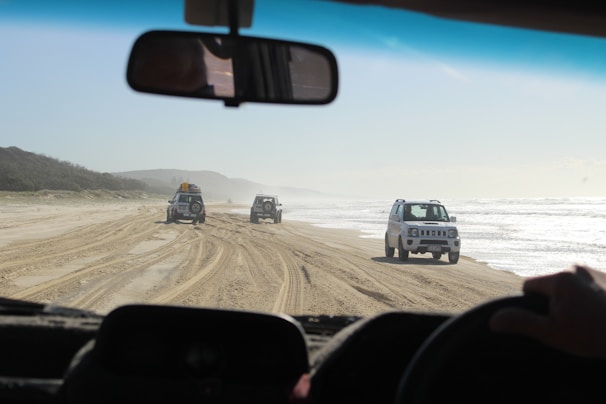 A convoy of 4x4 vehicles driving along a coastal road near the Emerald Sea with turquoise waters visible.
