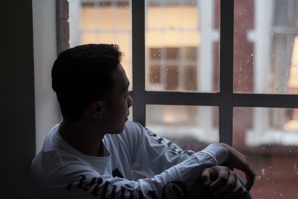 shallow focus photo of man in white long-sleeved shirt beside window
