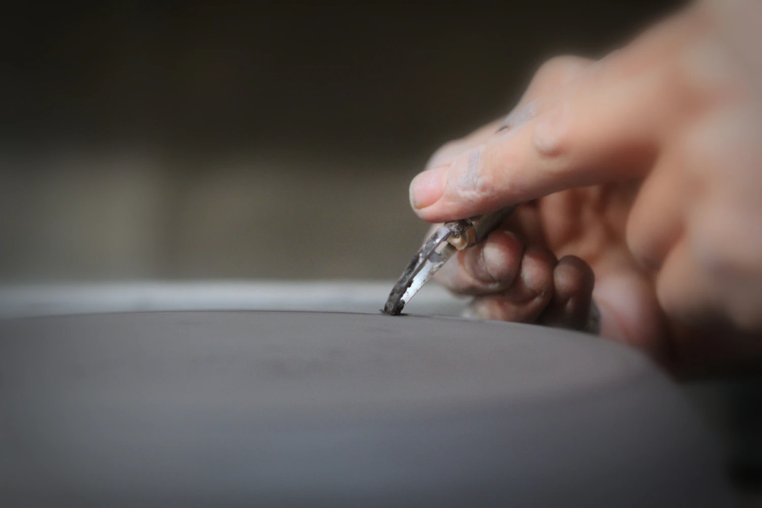 A hand steadying a graver against a turning workpiece, the background thrown out of focus