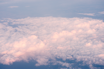 A vast expanse of soft, fluffy clouds with a gentle pink tint, possibly captured during sunrise or sunset. The clouds appear dense, creating a dreamy and serene atmosphere high above the earth.