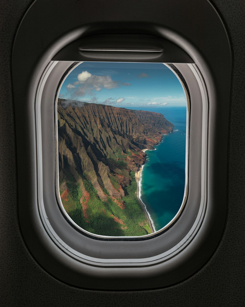 ein Flugzeugfenster mit Blick auf das Meer und die Berge