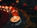 Small candles are lit in a dimly lit setting, surrounded by vibrant marigold flowers and colorful flower petals. The ambiance is warm and inviting, with the flickering candlelight casting soft shadows.
