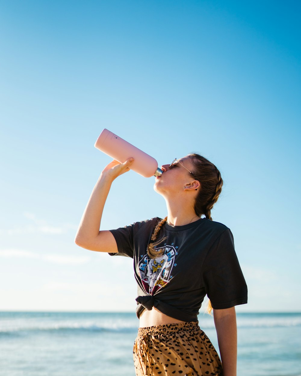 mujer bebiendo agua usando una botella rosa al lado del mar durante el día
