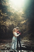 A couple embracing tenderly in a forest clearing with sunlight filtering through the leaves.