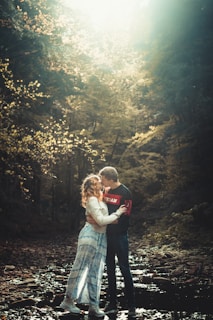 A couple embracing tenderly in a sunlit forest clearing with wildflowers around them.