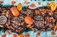 A vibrant and colorful seafood feast is displayed, featuring large crabs, shrimp, and mussels surrounded by rice and garnished with sliced mangoes and watermelon. Various grilled meats and a dish of dipping sauce are arranged on wooden platters, creating an inviting and appetizing arrangement.