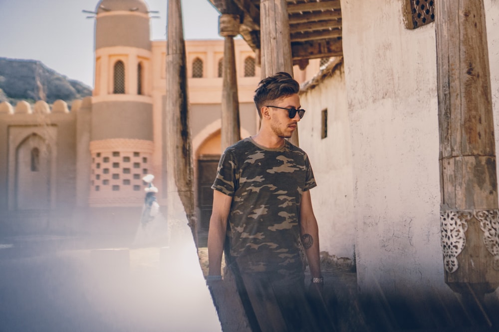 man in camouflage t-shirt walking beside wall
