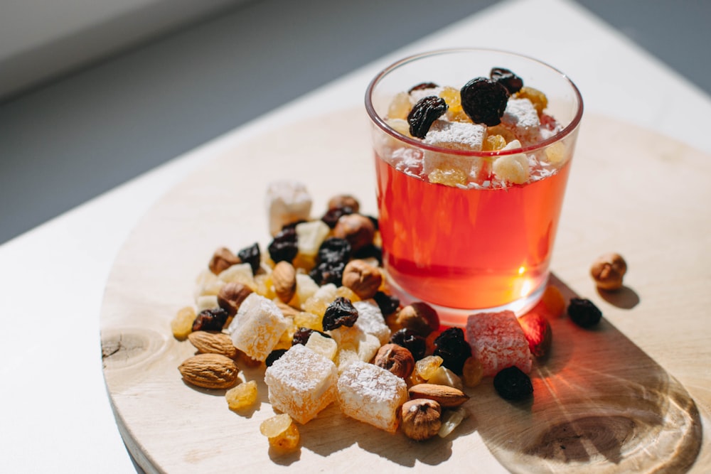 a wooden plate topped with a cup filled with fruit and nuts