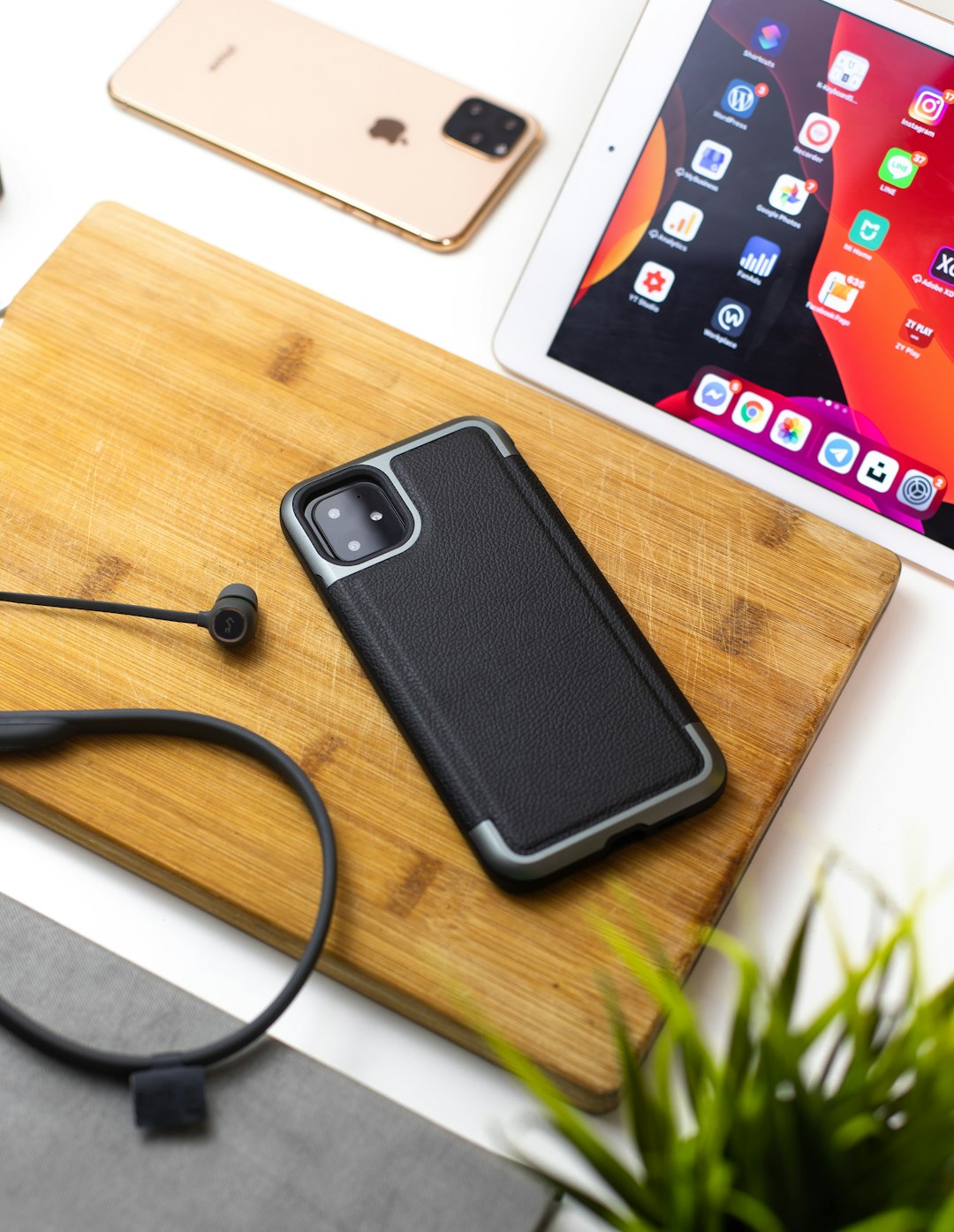 iPhone 11 on wood chopping board beside iPad and rose gold iPhone 11