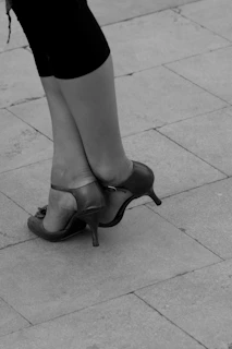 Close-up of a luxury female model’s feet adorned in sleek black heels with gold accents on a marble floor