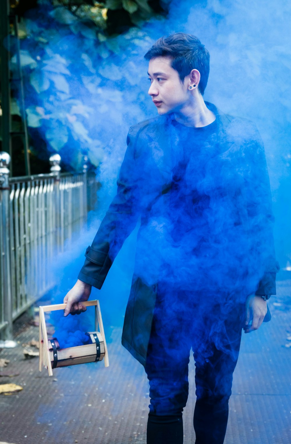 man wearing black jacket holding wooden box with blue smoke coming out