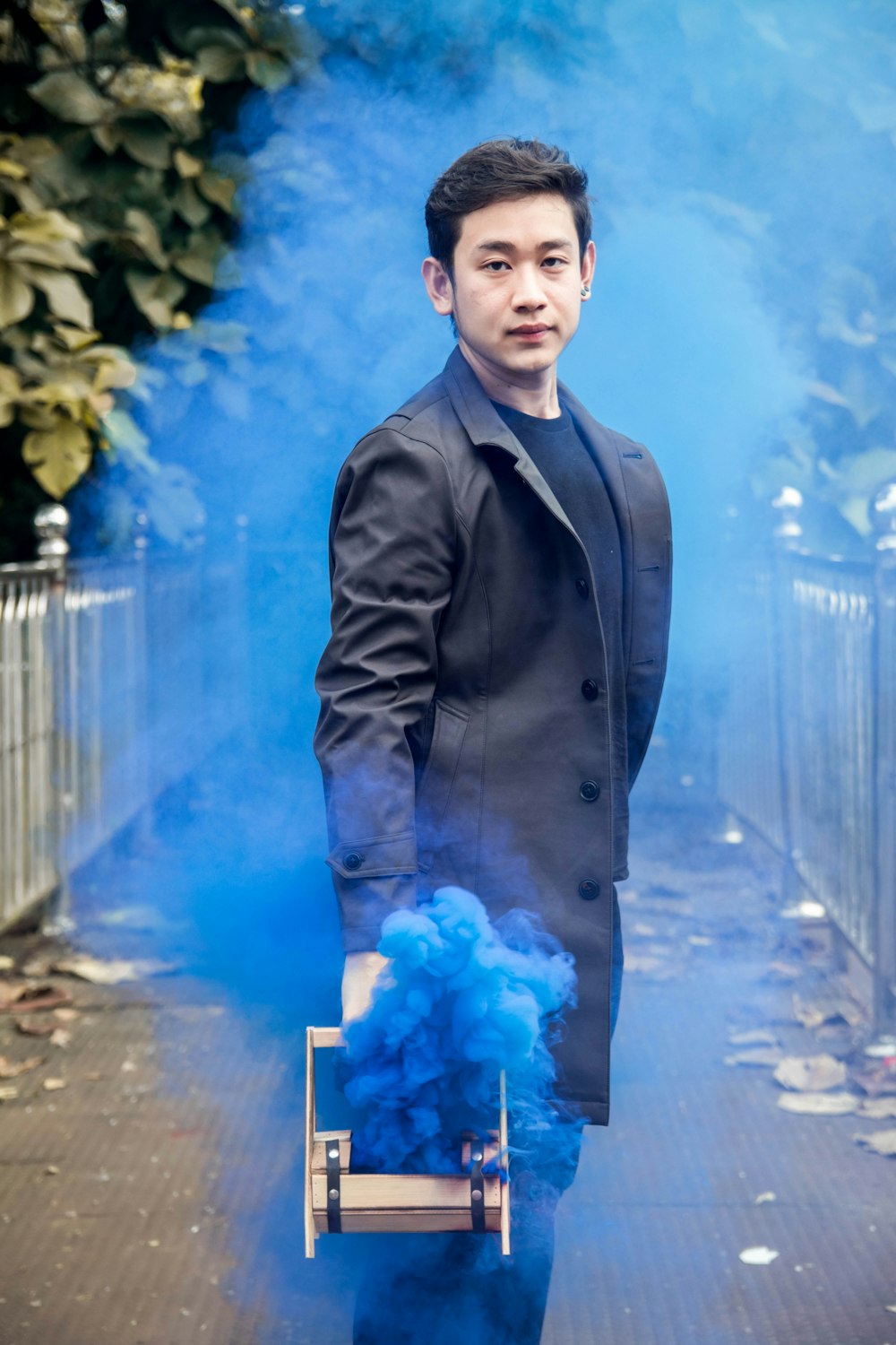 man in gray coat holding machine emitting blue smoke