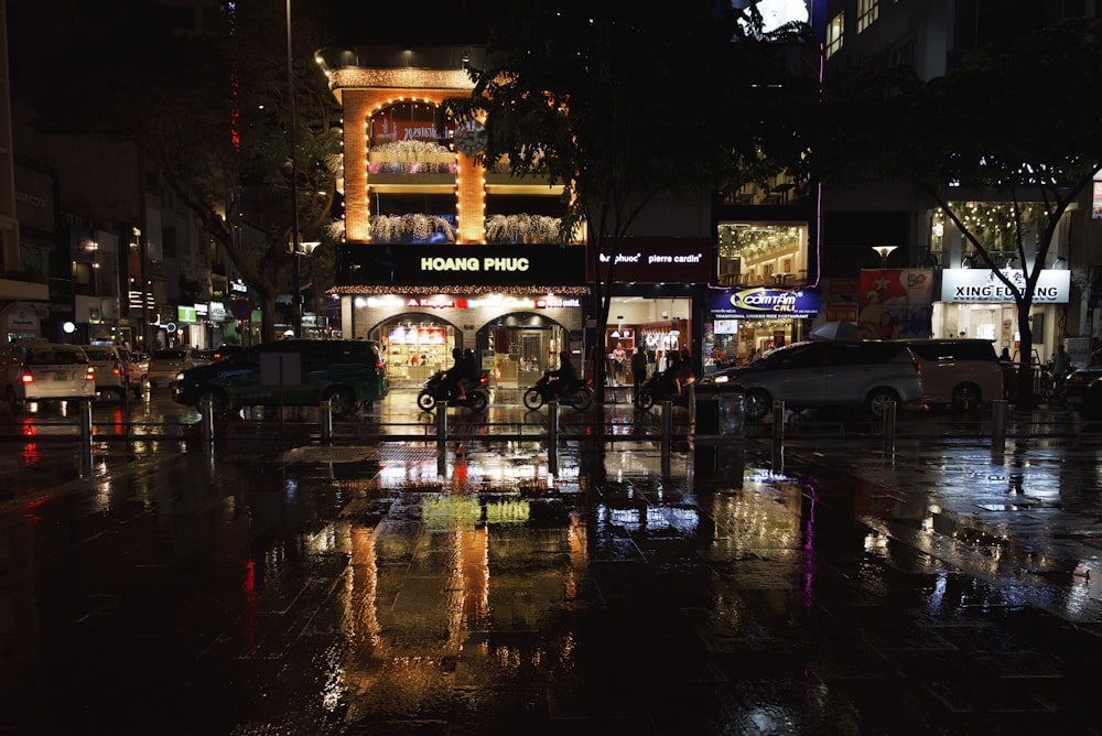 people walking on pathway near buildings and different vehicles on road during night time