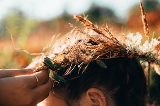 A close-up of hands weaving a wreath of wildflowers and ivy under a golden sunset.