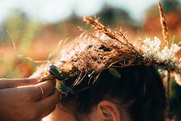 A close-up of hands weaving a wreath of wildflowers and ivy under a golden sunset.