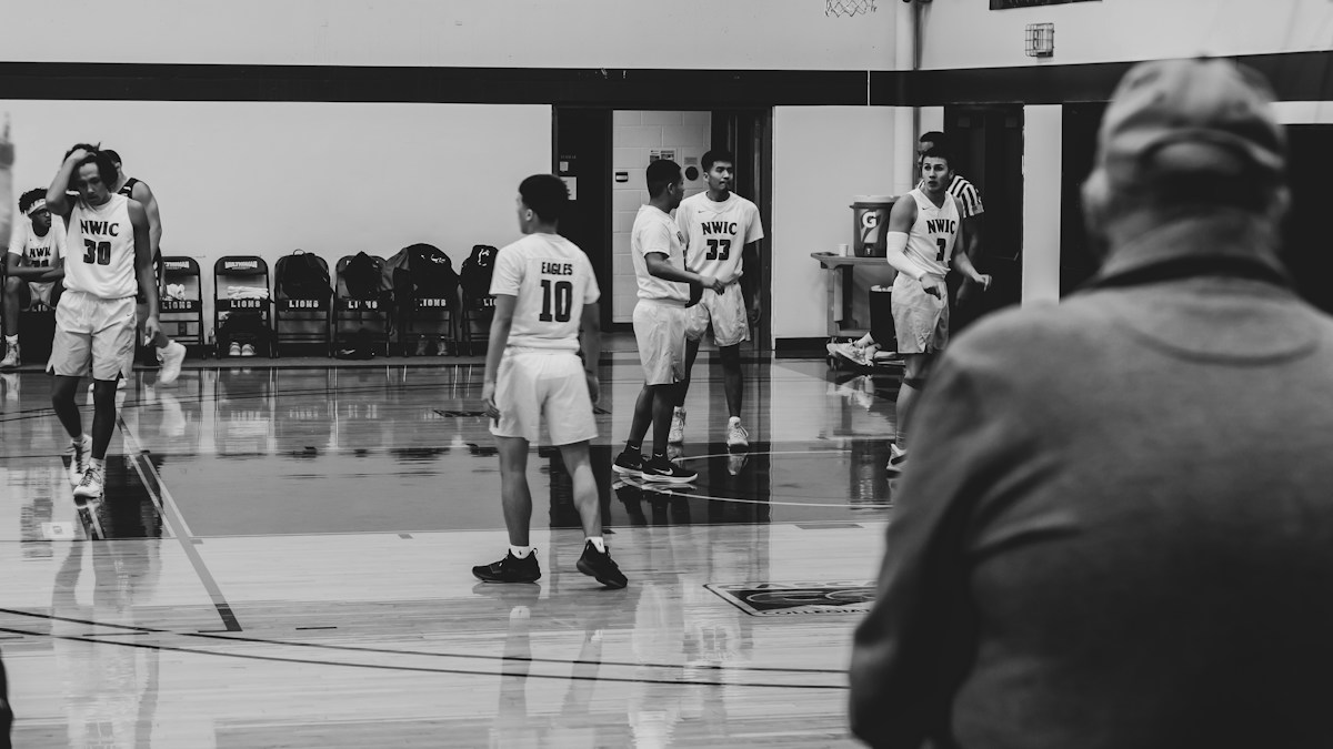 Grayscale photo of a coach giving a pep talk to youth players on a basketball court, emphasizing leadership and communication.